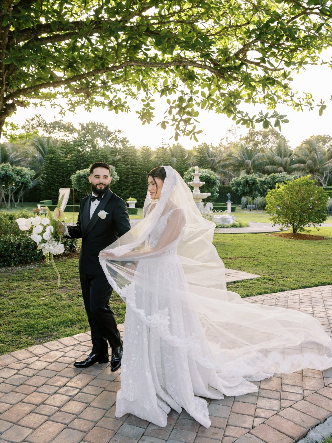 Bride and groom with flowing veil on the garden path at Cinco Farm wedding venue in Miami