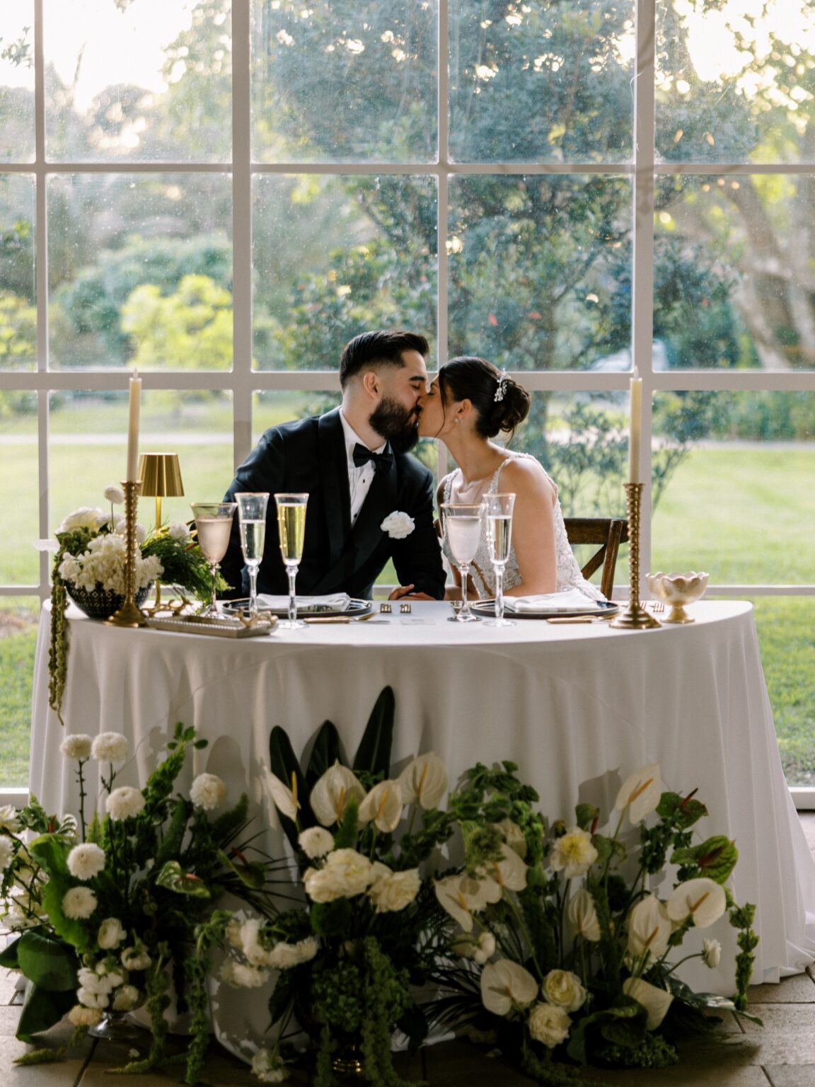 Couple kissing at their sweetheart table in the glasshouse reception at Cinco Farm